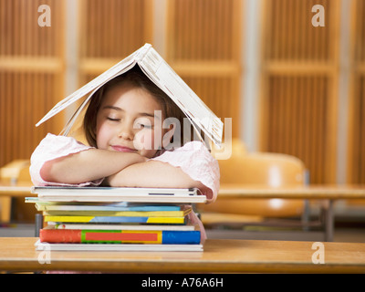 La ragazza (4-7) una scrivania, poggiando sulla pila di libri a occhi chiusi Foto Stock