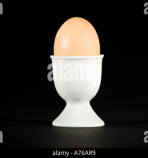 Tutto un uovo sodo in un eggcup bianco puro su sfondo nero. Foto Stock