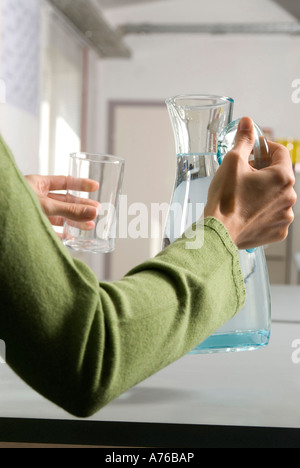 Giovane donna versando acqua dalla brocca in vetro, metà sezione, close-up Foto Stock