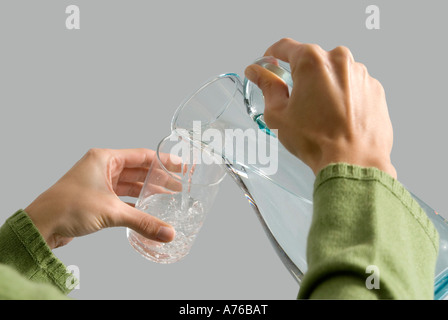 Giovane donna versando acqua dalla brocca in vetro, close-up Foto Stock