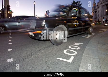 Basso ampio angolo di flash e il riempimento di una tradizionali taxi neri guida intorno a un angolo in Trafalgar Square con motion blur. Foto Stock