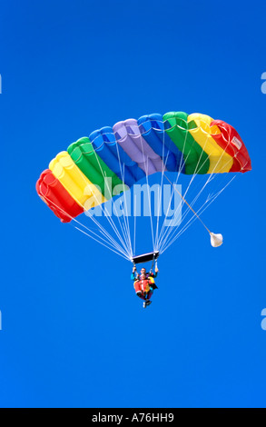 Buddy paracadutisti galleggiando giù nel cielo con un arcobaleno paracadute colorato ed un cielo blu sullo sfondo. Foto Stock