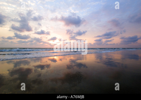 Un colorato tramonto e nuvole riflettono in acqua receeding sulla spiaggia. Foto Stock