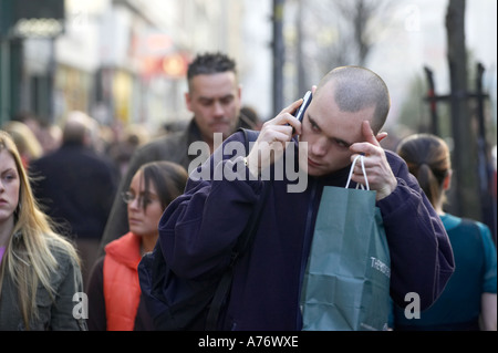 I giovani con il suo capo rasato uomo sul cellulare in folla mentre fuori lo shopping natalizio a Belfast per la Vigilia di Natale Irlanda del Nord Foto Stock