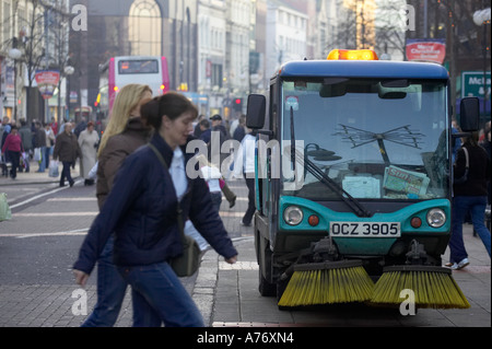 I pedoni a piedi passato macchina spazzatrice stradale in Royal Avenue durante lo shopping natalizio a Belfast per la Vigilia di Natale Foto Stock