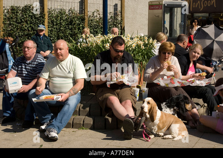 Gruppo di persone sovrappeso seduti e mangiare patatine fast food nel sole, REGNO UNITO Foto Stock