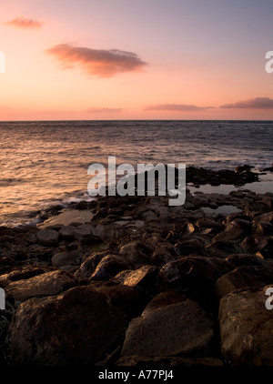 Un bel golden glow scende sulle rocce dei Giganti Causeway Irlanda del Nord come il sole tramonta su un oceano di calma Foto Stock