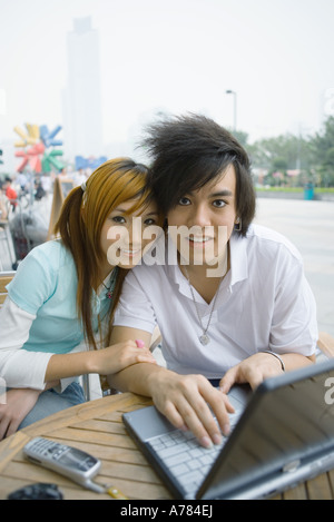 Coppia adolescenti seduti all'aperto, utilizzando laptop, sorridente in telecamera Foto Stock