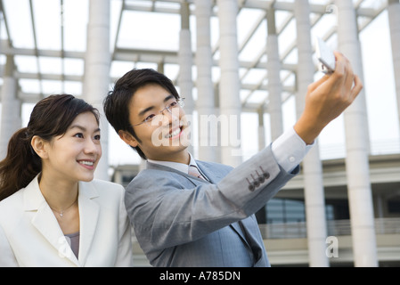 Imprenditore in piedi accanto al collega di sesso femminile, prendendo foto con il telefono cellulare Foto Stock