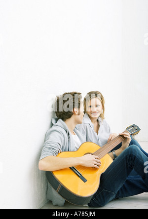 Giovane uomo e donna seduta sul terreno, l'uomo a suonare la chitarra Foto Stock