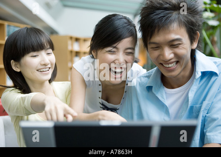 Tre amici utilizzando il computer, ridendo Foto Stock