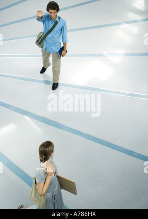 Ragazzo adolescente che indossa la borsa messenger sventolare a femmina amico, a lunghezza piena, ad alto angolo di visione Foto Stock