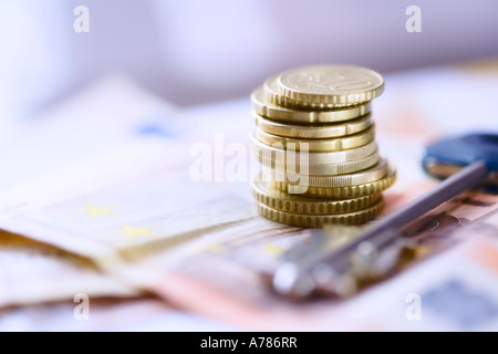 Colonna di piccole dimensioni delle monete metalliche in euro e la chiave sulle banconote in euro Foto Stock