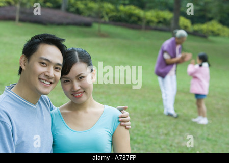 Coppia sorridente in telecamera, senior donna e bambina in background Foto Stock