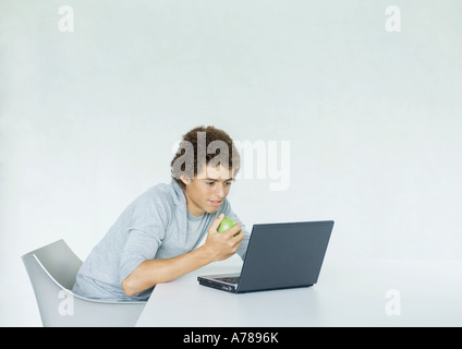 Ragazzo adolescente utilizzando laptop e mangiare apple Foto Stock