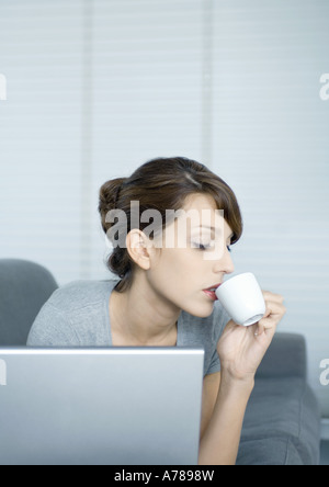 Giovane donna sul lettino, utilizzando laptop e di bere il caffè Foto Stock