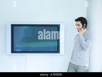 Uomo appoggiato a parete tramite telefono, accanto al televisore widescreen Foto Stock