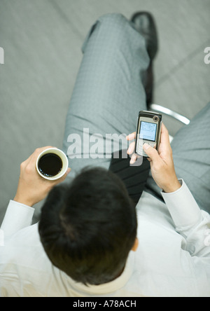 Imprenditore utilizzando smart phone, tenendo tazza di caffè Foto Stock