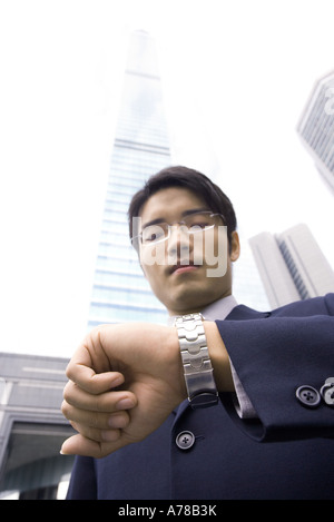 Imprenditore il controllo permanente di tempo su un orologio da polso, grattacielo in background Foto Stock