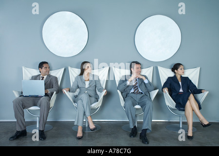 I dirigenti aziendali seduti nella fila di sedie, guardando fuori del telaio Foto Stock