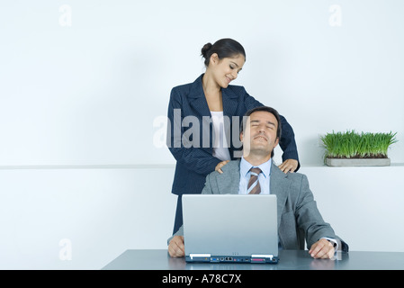 Imprenditore avente massaggio della spalla dal collega femmina Foto Stock