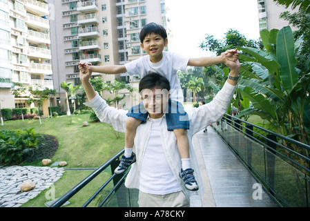 Ragazzo a cavallo sul padre di spalle, vista frontale, sorridente in telecamera Foto Stock