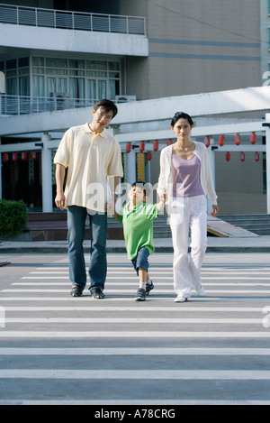 Ragazzo attraversando crosswalk, mano nella mano con i genitori a piena lunghezza Foto Stock