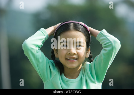 La ragazza con le mani sul capo, sorridente in telecamera Foto Stock