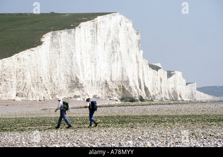Scogliere bianche di gesso paesaggio Seven Sisters sulla costa della Manica due escursionisti che attraversano la spiaggia di ciottoli accanto al fiume Cuckmere East Sussex Regno Unito Foto Stock