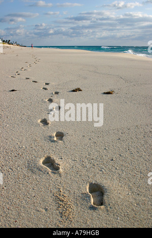 Spiaggia solitaria a piedi. Una lunga linea di impronte profonde nella sabbia portano a una piccola figura camminare da solo su una spiaggia di attualità Foto Stock