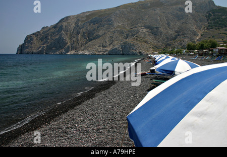 Ombrelloni sulla spiaggia: blu e bianca spiaggia ombrelloni e sedie lungo la spiaggia rocciosa di un paio di nuotatori nell acqua Foto Stock