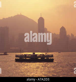 Il famoso Star Ferry vele lungo il lungomare nebuloso del quartiere centrale al tramonto con il Victoria Peak Hill al di là dell'Isola di Hong Kong Foto Stock