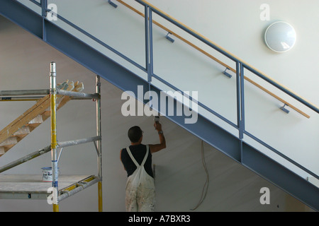 Pittore e decoratore facendo i tocchi finali al di sotto di una scala. Foto Stock