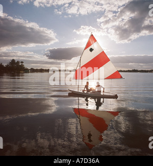 Giovane rilassante sulla barca a vela nel lago al tramonto Foto Stock