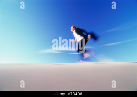 Imprenditore in esecuzione attraverso dune di sabbia con valigetta Foto Stock