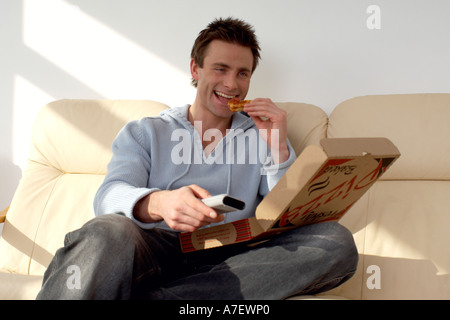 Uomo seduto su un divano a mangiare la pizza e guardare la televisione Foto Stock