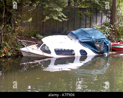 Il primo piano di una barca a motore ormeggiata ribaltata e parzialmente affondata apparentemente abbandonata sul canale di Basingstoke nel Surrey, Inghilterra, Regno Unito Foto Stock