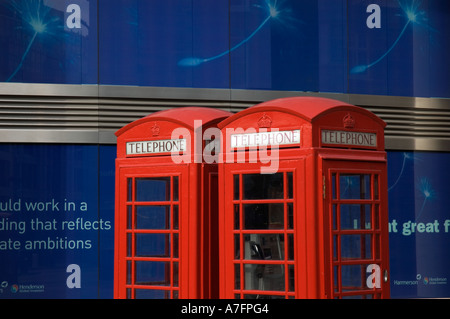 Due tradizionali cabine telefoniche rosse contro blu pubblicità su ufficio moderno edificio, London, England, Regno Unito Foto Stock