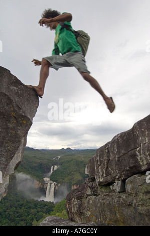 Una guida salti fra 2 formazioni rocciose nella Chapada dos Veadeiros con la 120 e 80 metri di cascata in background. Foto Stock