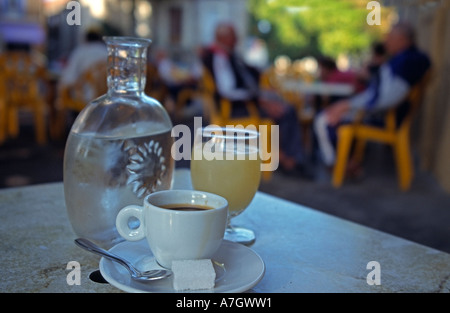 Tazza piena di caffè espresso una bottiglia di acqua minerale e un bicchiere di pastis anis schnaps booze antipasto gente seduta in background Foto Stock