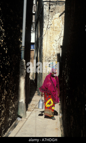 Il swahili donna a piedi attraverso uno dei vicoli stretti nella città vecchia di Lamu, Kenya Foto Stock