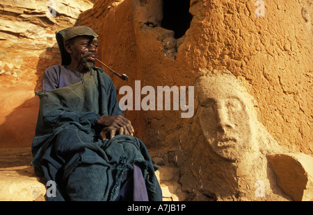 Hogon, leader spirituale di fumare un tubo nella sua scogliera scolpita home, Ende village, Paese Dogon del Mali Foto Stock