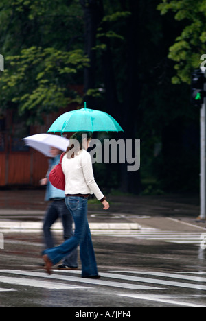Giovane donna attraversare una strada trafficata in corrispondenza di un incrocio di Zebra sotto la pioggia Foto Stock