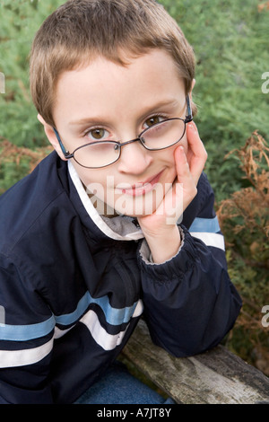 Ritratto di giovane ragazzo che indossa gli occhiali e giacca leggera inclinazione all'aperto il suo mento nella sua mano aperta il gomito su una rampa di recinzione Foto Stock