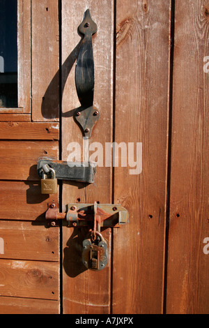 Porta a capannone da giardino in legno fissata con vecchi lucchetti e bulloni alla luce del sole. Foto Stock