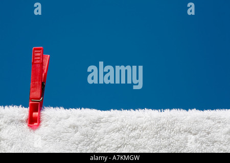 Molletta da bucato su un asciugamano bianco e linea di lavaggio contro un cielo blu Foto Stock