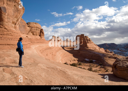 Donna in piedi su Entrada battuta di arenaria e guardando il Delicate Arch Arches National Park vicino a Moab nello Utah Stati Uniti d'America Foto Stock