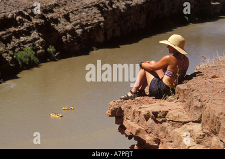 Escursionista femmina seduto su un promontorio roccioso che si affaccia su due zattere di meandro lungo il Fiume Colorado USA Utah Foto Stock