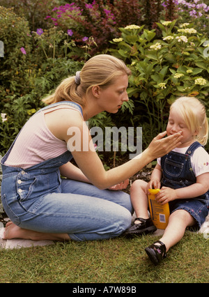 Madre che applica crema solare, sunsreen, al viso di un bambino nel giardino, Regno Unito Foto Stock