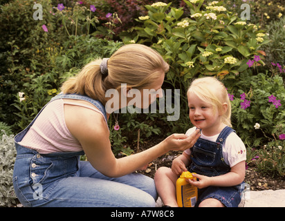 Madre che applica crema solare crema solare al viso di un bambino in giardino, Regno Unito Foto Stock